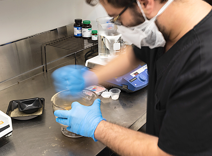 man wearing a mask crushing pills in a lab