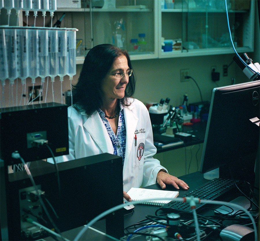 A portrait photograph of Michaela Jansen, PharmD, PhD in a white laboratory coat working on/glancing at her computer as she researches information on neurological disorders