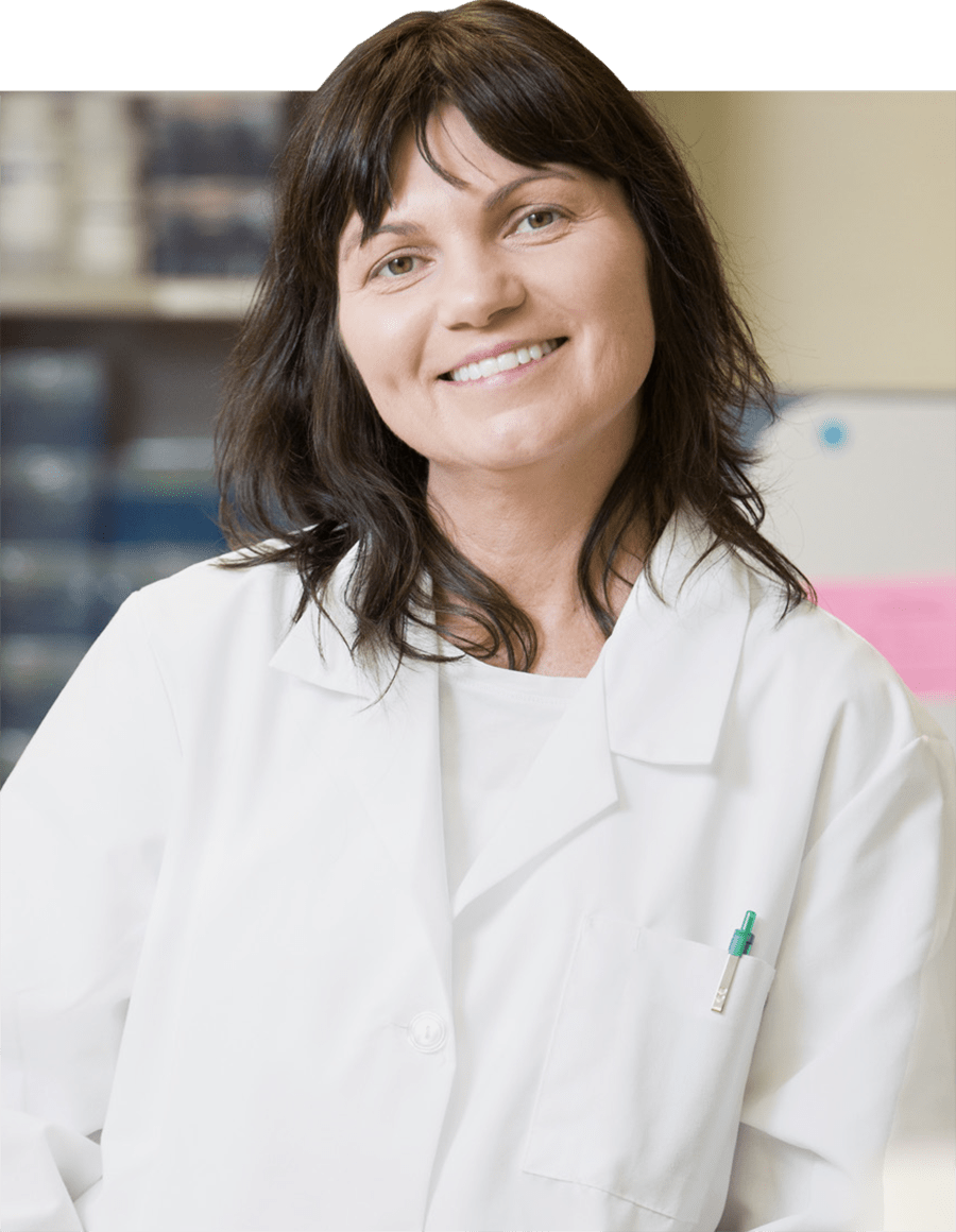 A portrait headshot photograph of Magdalena Karbowniczek (MD, PhD) smiling in a white medical laboratory coat with a light green pen tucked in her left pocket of the coat