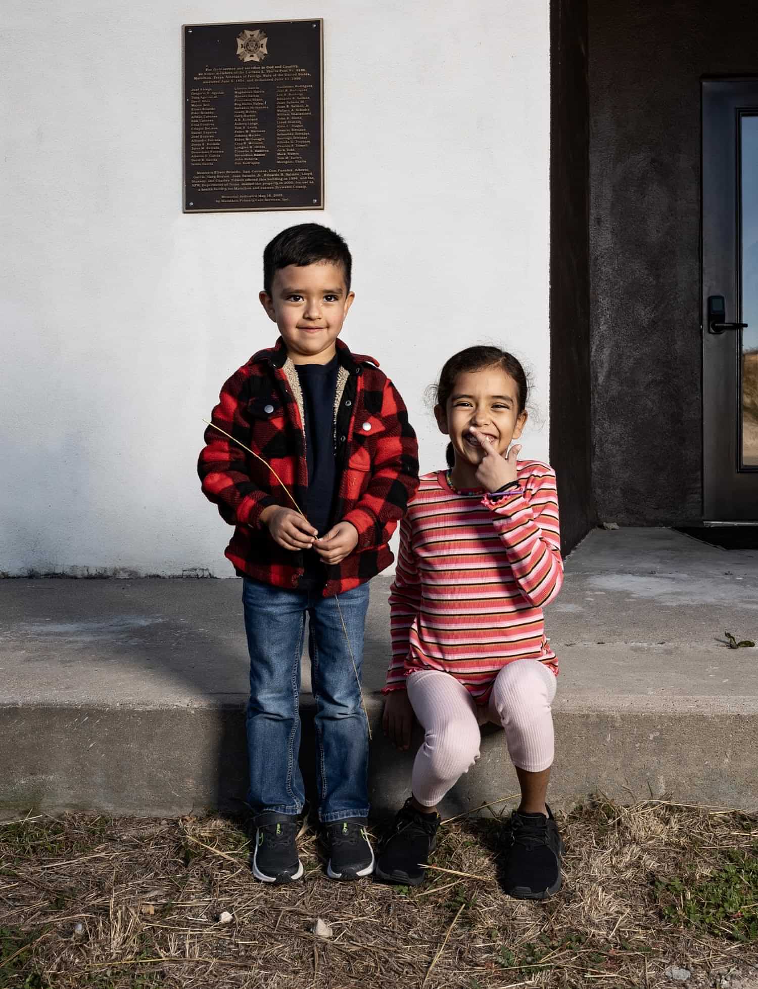 a smiling young boy stands next to a smiling young girl sitting on the step of the Marathon Health Center