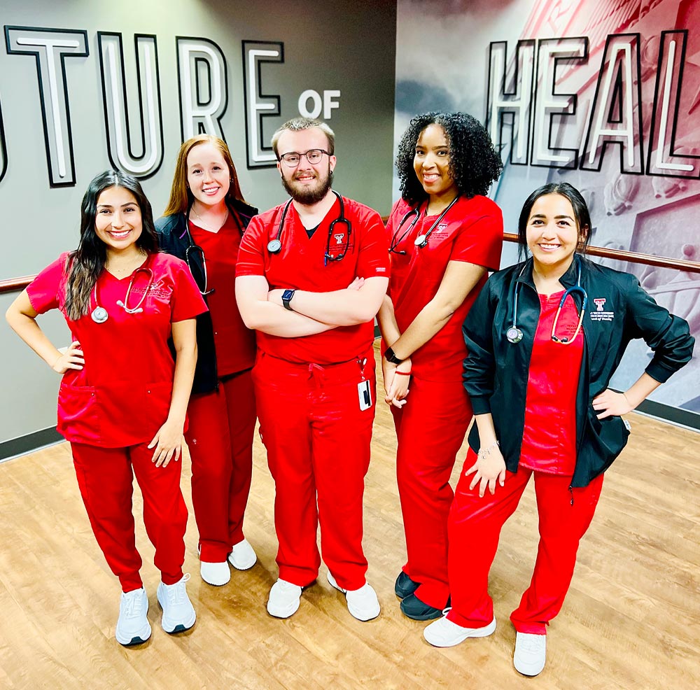 four female and one male nursing student, all wearing bright red Texas Tech scrubs, stand together and smile for a group photo