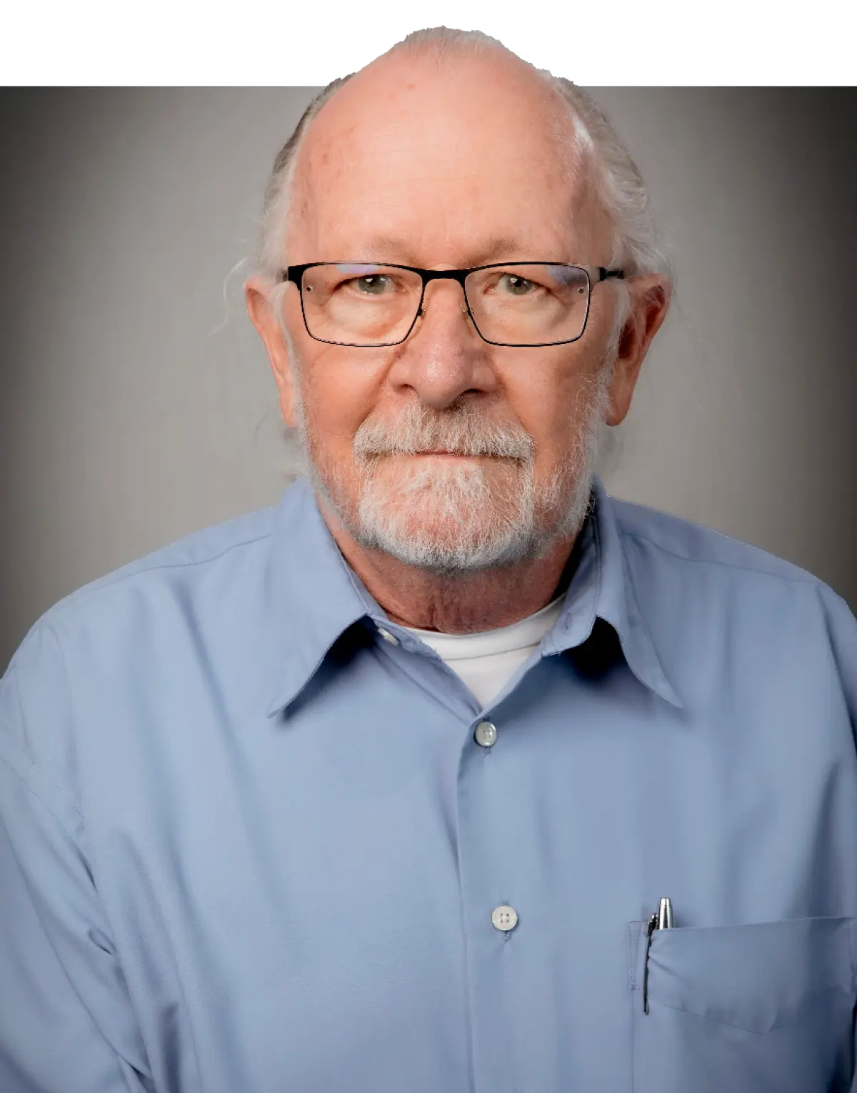 Portrait photograph close-up headshot of Joe Fralick (PhD) grinning in black outer frame see through prescription glasses and a light sky blue button-up dress shirt with a chrome-colored pen in his small pocket opening embedded into the dress shirt