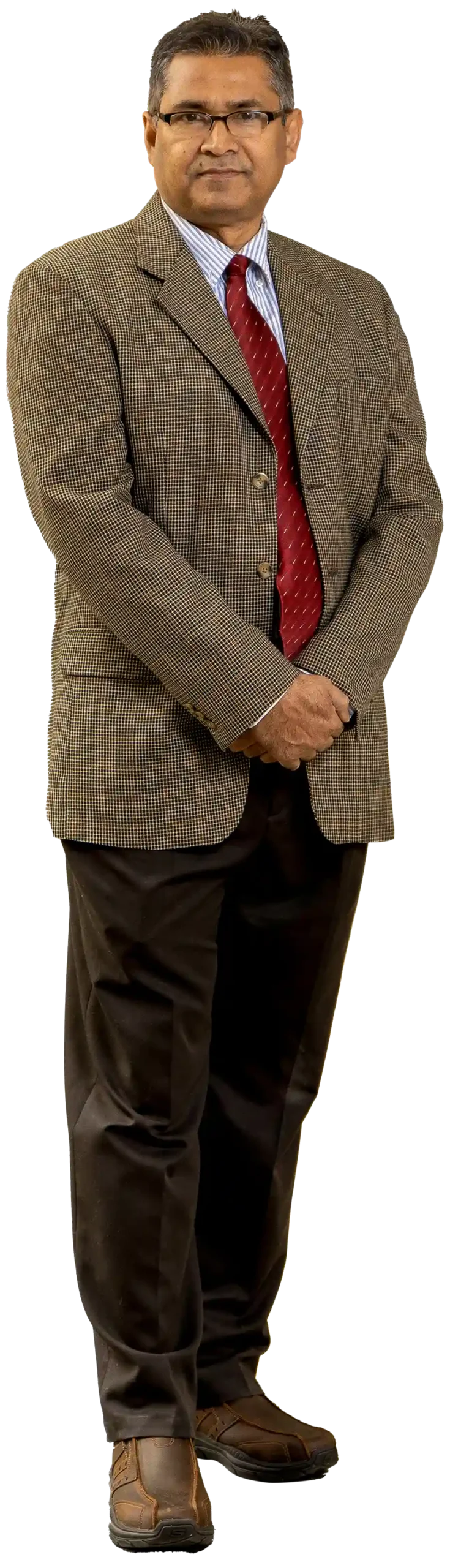 Portrait photograph perspective of Hafiz Khan (PhD) grinning and posing/standing for a picture with dark black color outer frame prescription see through glasses in a faded rusty light beige colored business suit blazer coat with a white/light blue colored striped pattern button-up dress shirt underneath plus a dark red tie equipped also; He also has on dark brown dress slack pants and dark brown dress shoes as well while he rests one of his hands over the other hand