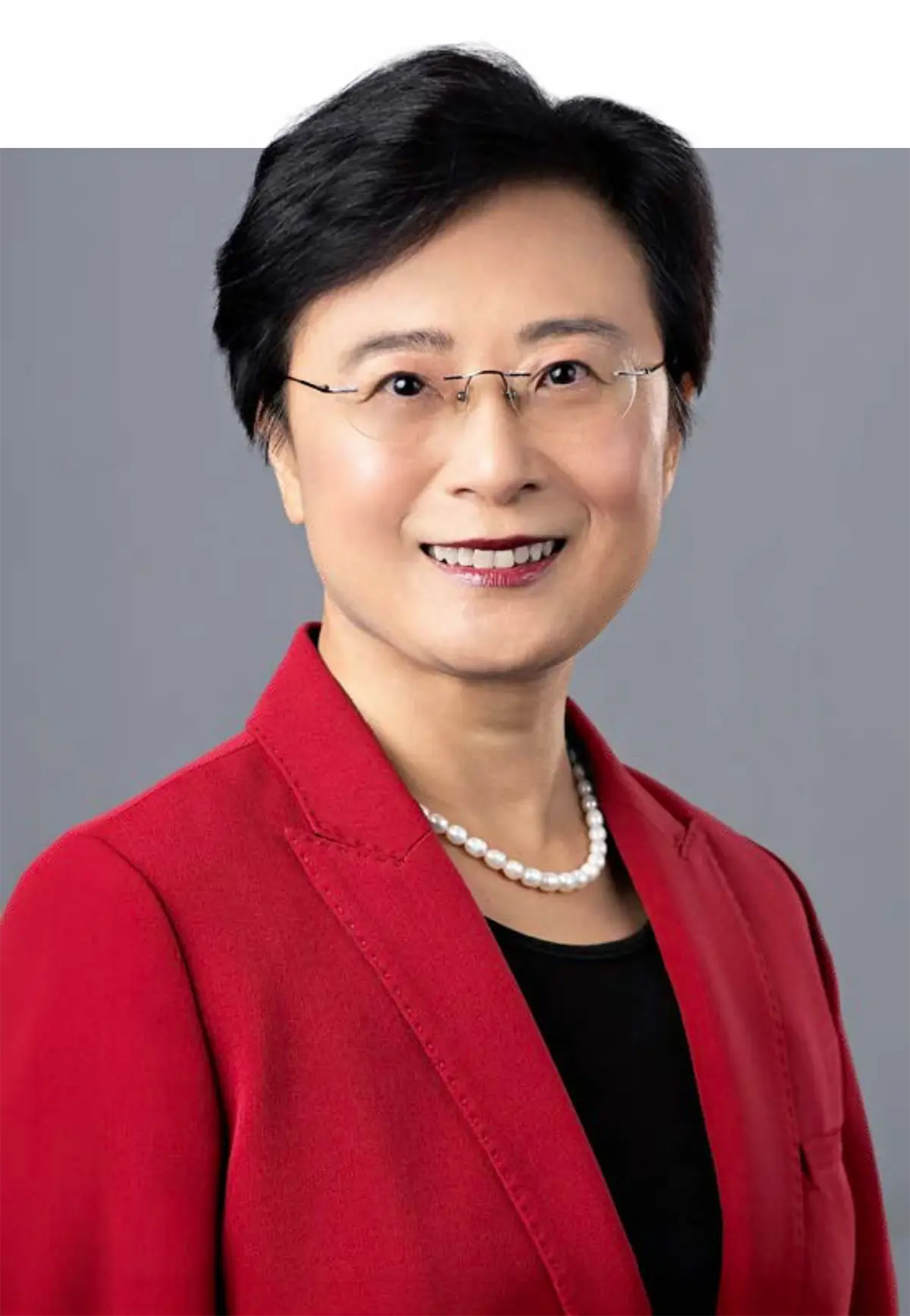 Portrait photograph headshot perspective of Holly Wei (PhD, RN) smiling in a bright red colored business suit blazer coat with a black blouse underneath and a white pearl style necklace around her plus she has on dark red lipstick as well as chrome-colored outer frame see through prescription glasses