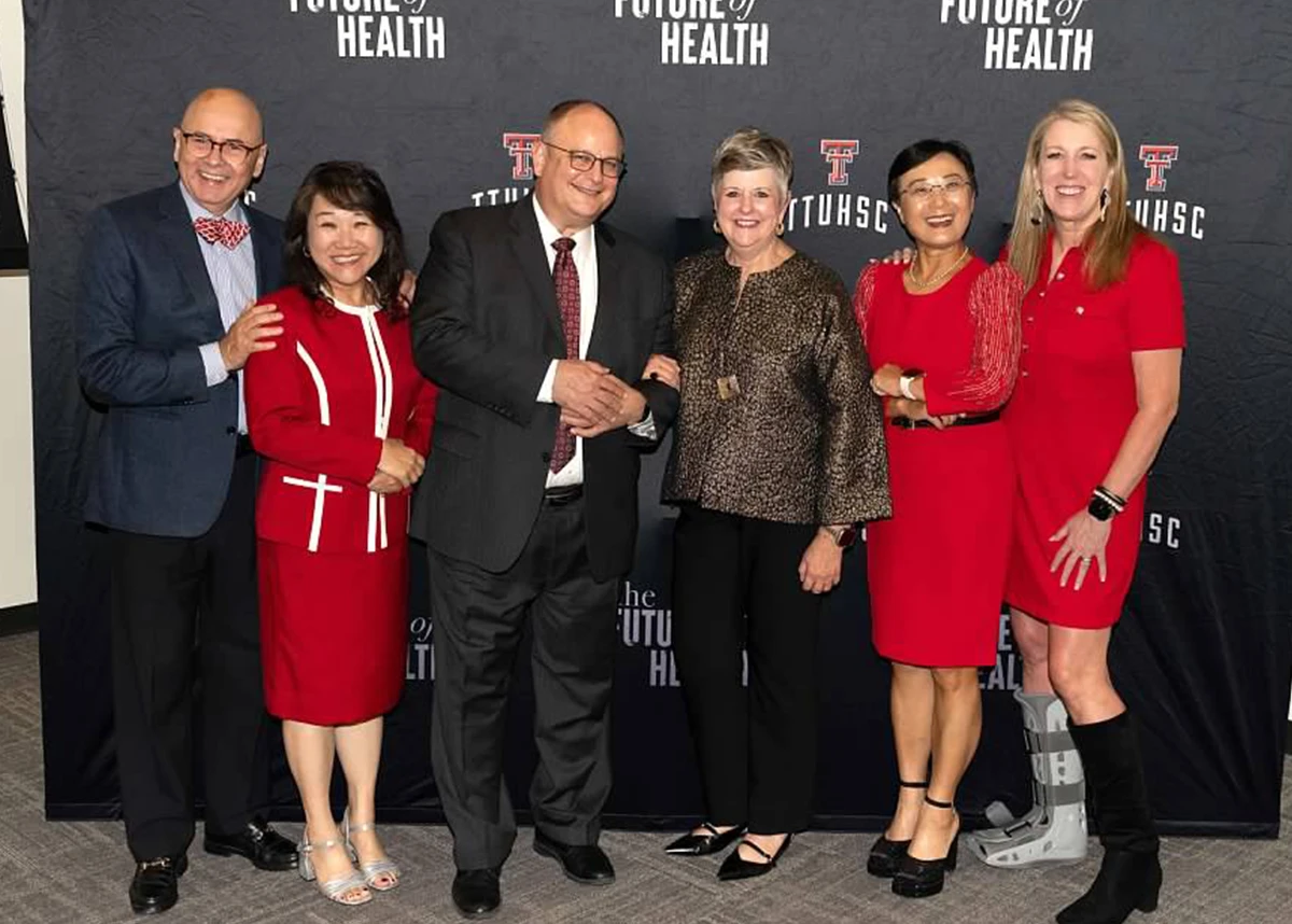 Group of seven formally dressed adults standing shoulder to shoulder in front of a TTUHSC “The Future of Health” backdrop at an alumni awards ceremony.