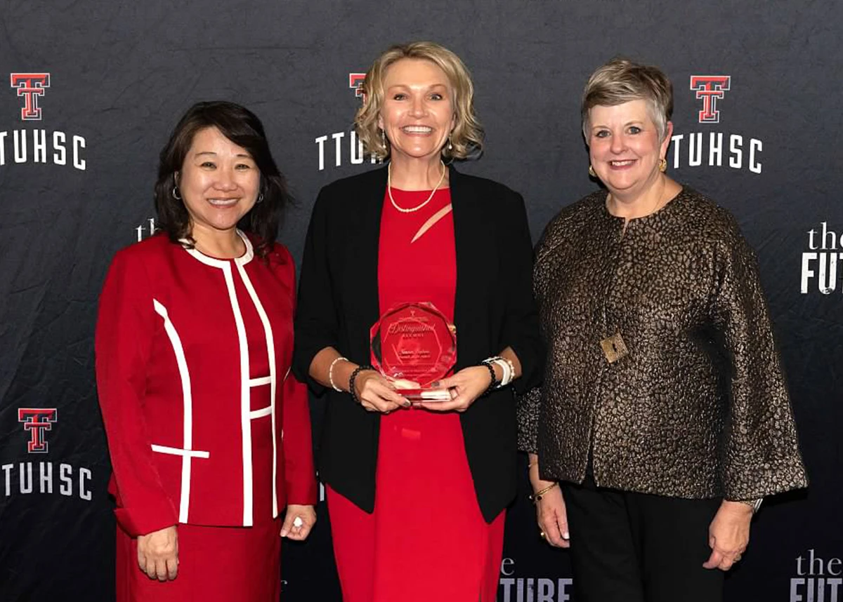 Three adults smiling and posing together in front of a TTUHSC “The Future of Health” backdrop, with one person holding a crystal alumni award.