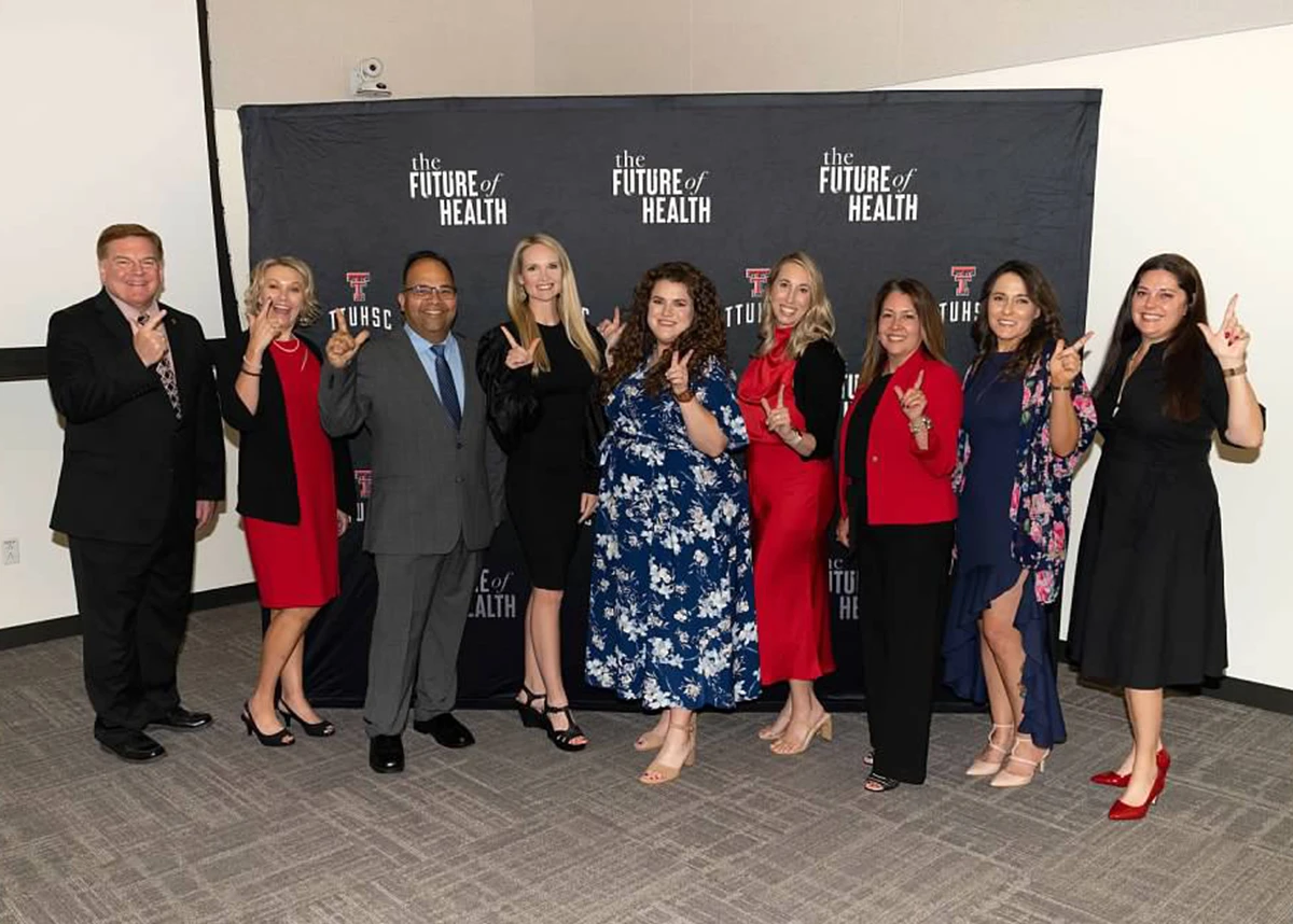 Large group of formally dressed attendees standing in front of a TTUHSC “The Future of Health” step-and-repeat backdrop, smiling and posing together at an alumni awards ceremony.