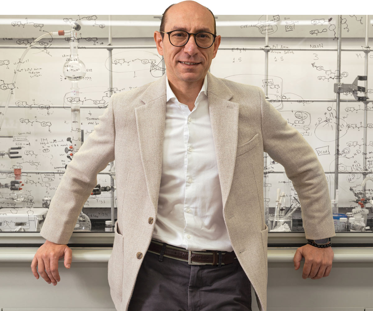 Mahmoud Salama Ahmed in a beige blazer in front of a whiteboard with chemical equations.