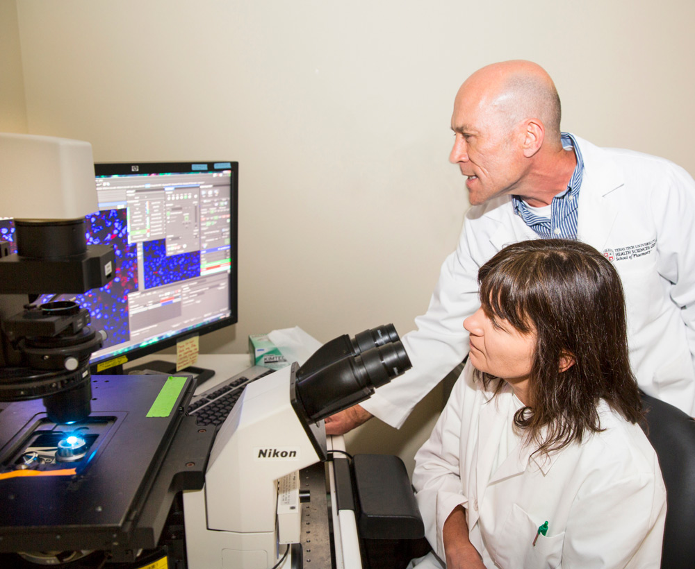 Two scientists working with a microscope and computer in a lab.