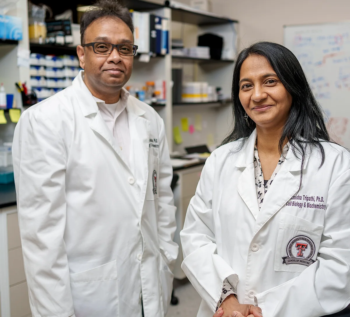 Srinivas Nandana and Manisha Tripathi standing in a research lab featuring medical equipment and a whiteboard with diagrams.