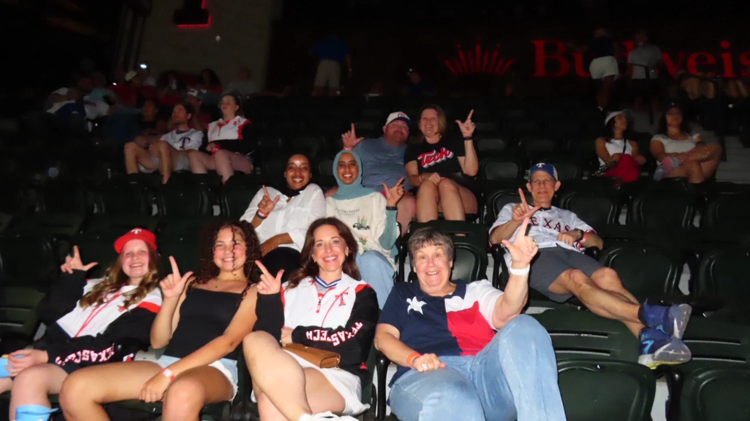 Texas Tech supporters make the Guns Up hand sign while seated at a baseball game.