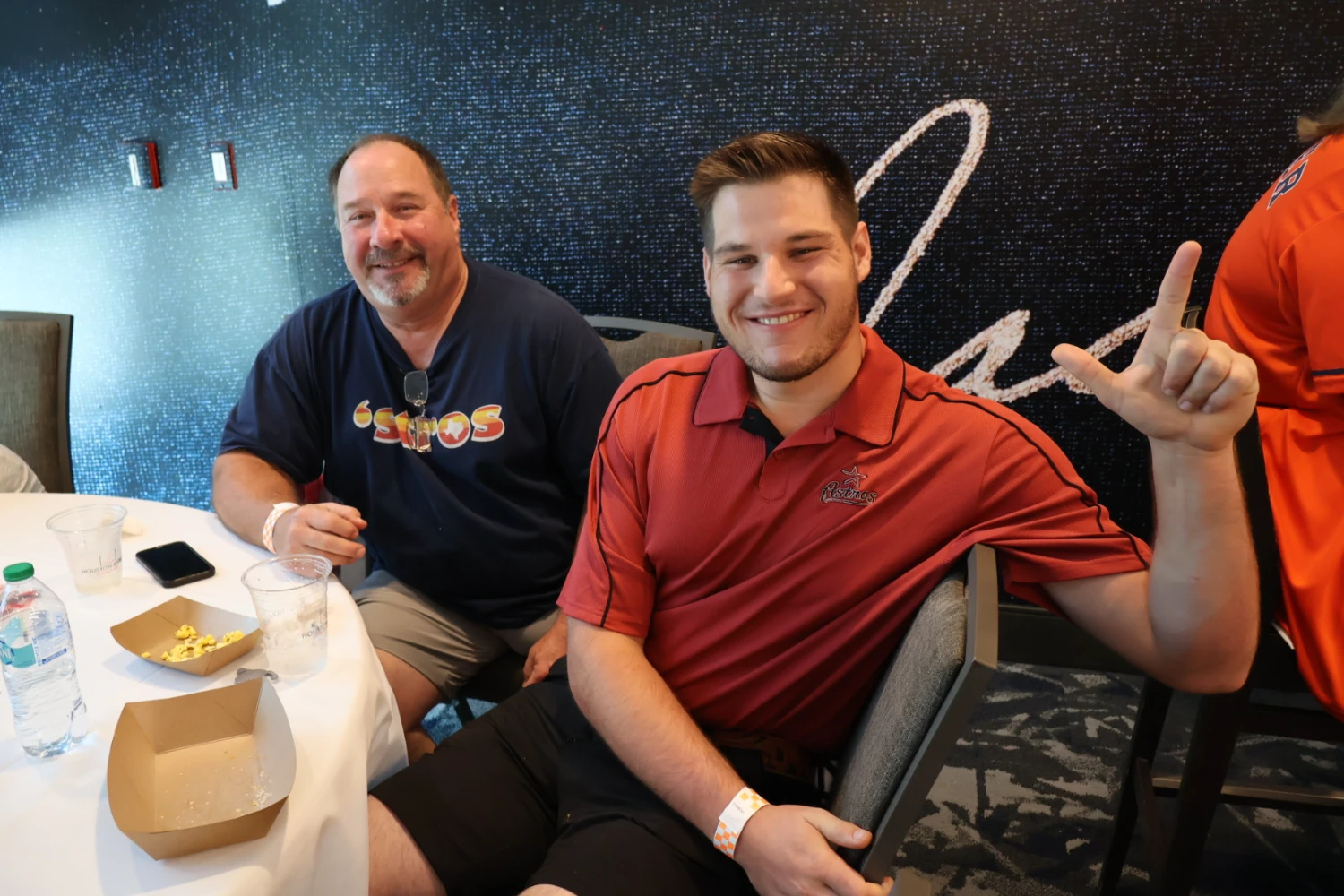 Two Houston Astros fans smile at a table, with one making the Guns Up hand sign.