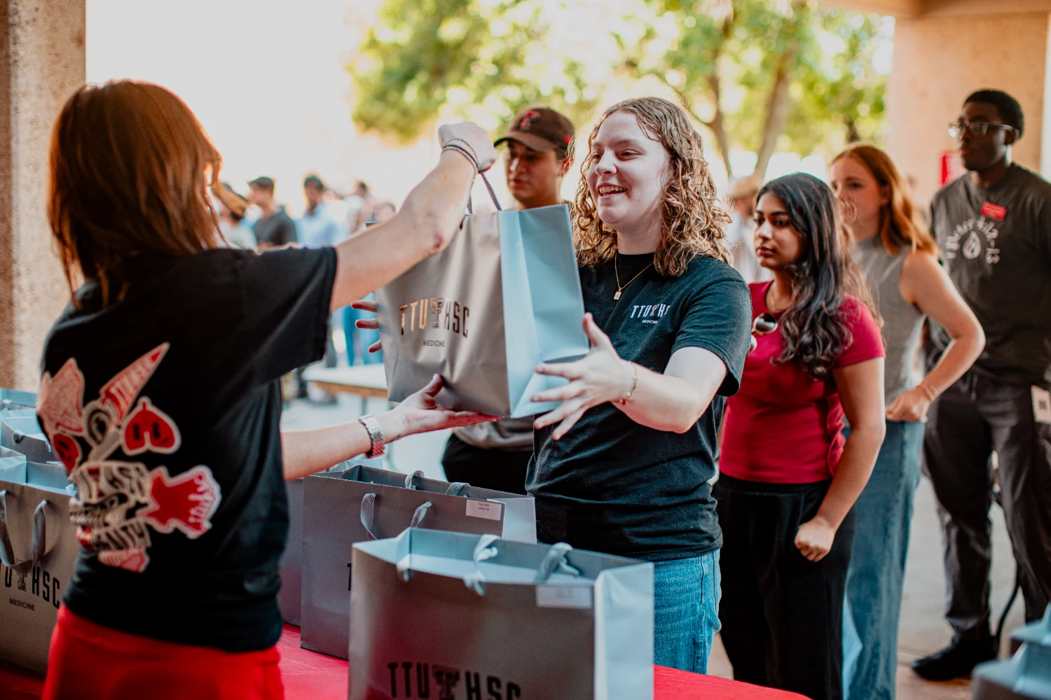 A student receives a TTUHSC Medicine welcome bag as other students wait in line.