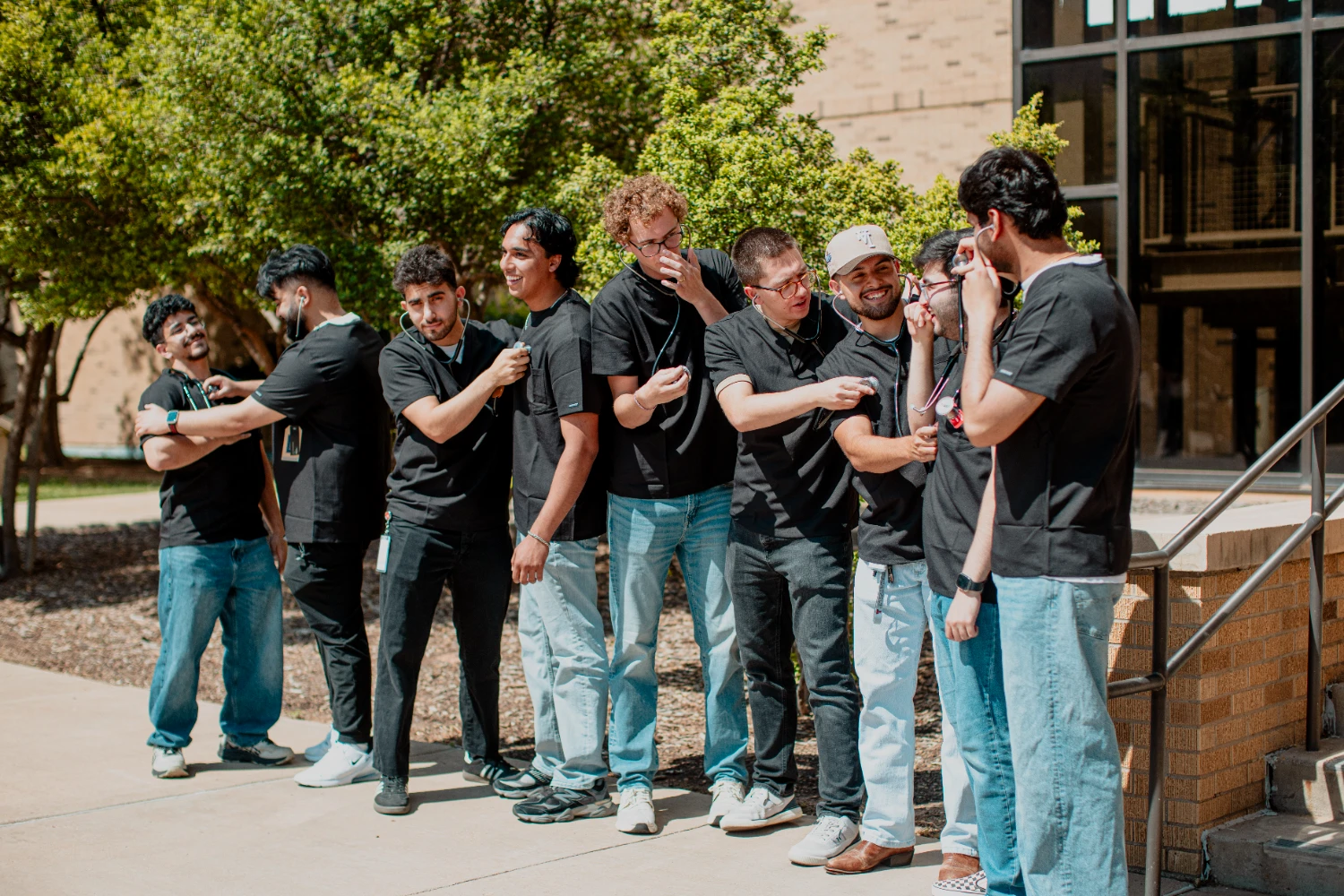 Medical students practice using stethoscopes on one another outside a campus building.