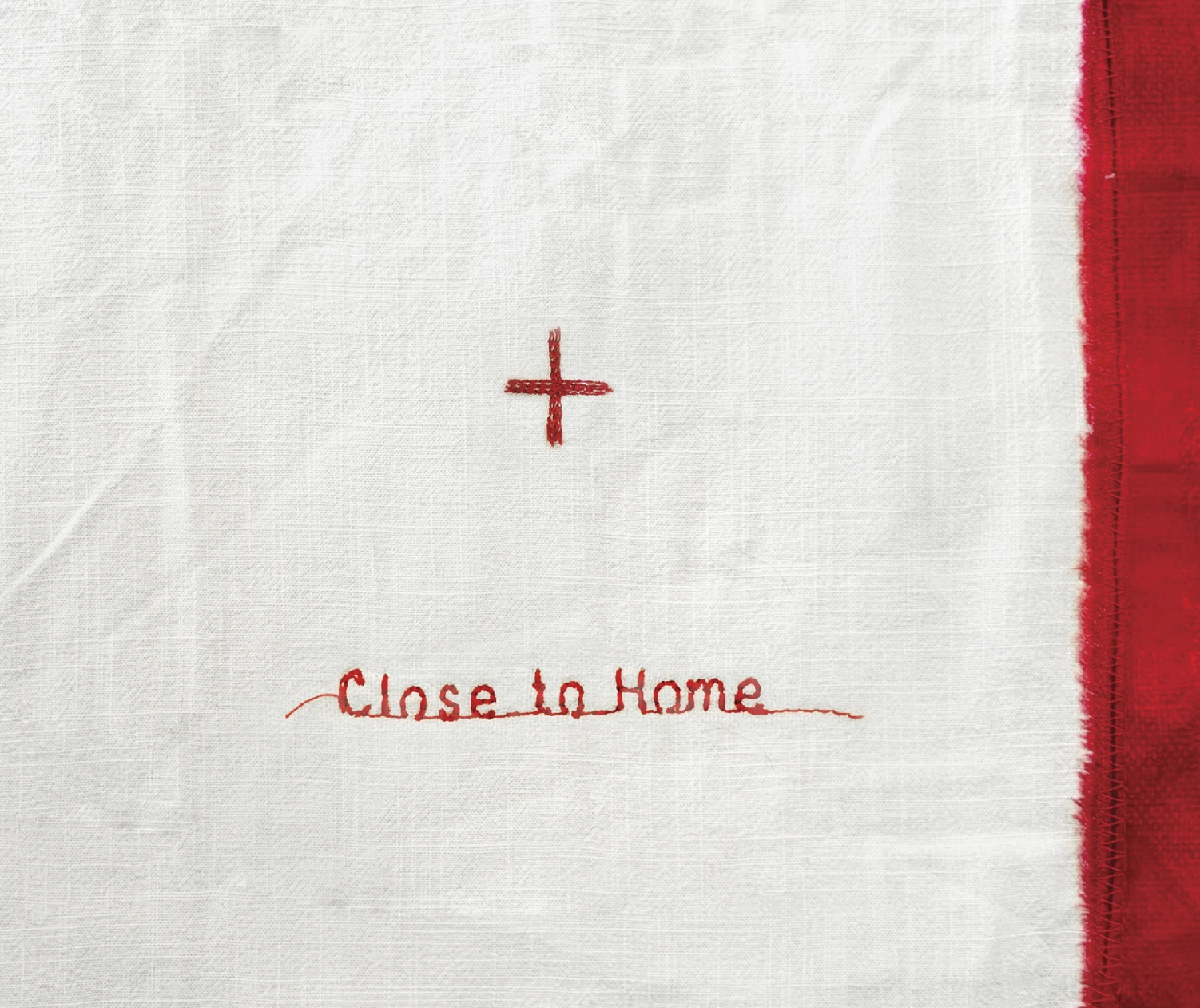 Quilted white fabric with red cross stitching and words that say close to home