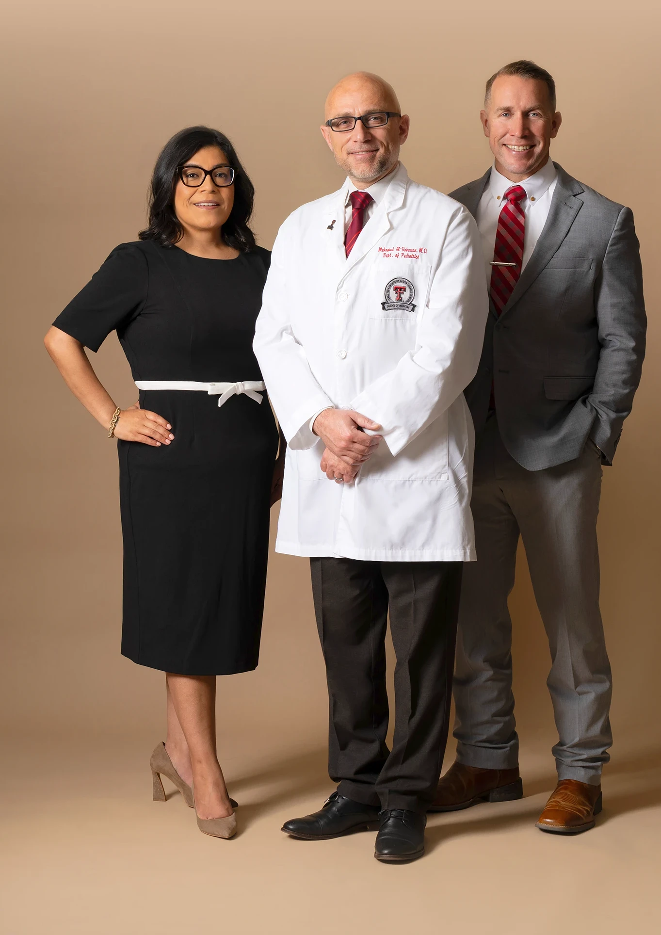 Three health care professionals, including a physician in a white coat, pose together against a neutral studio background.