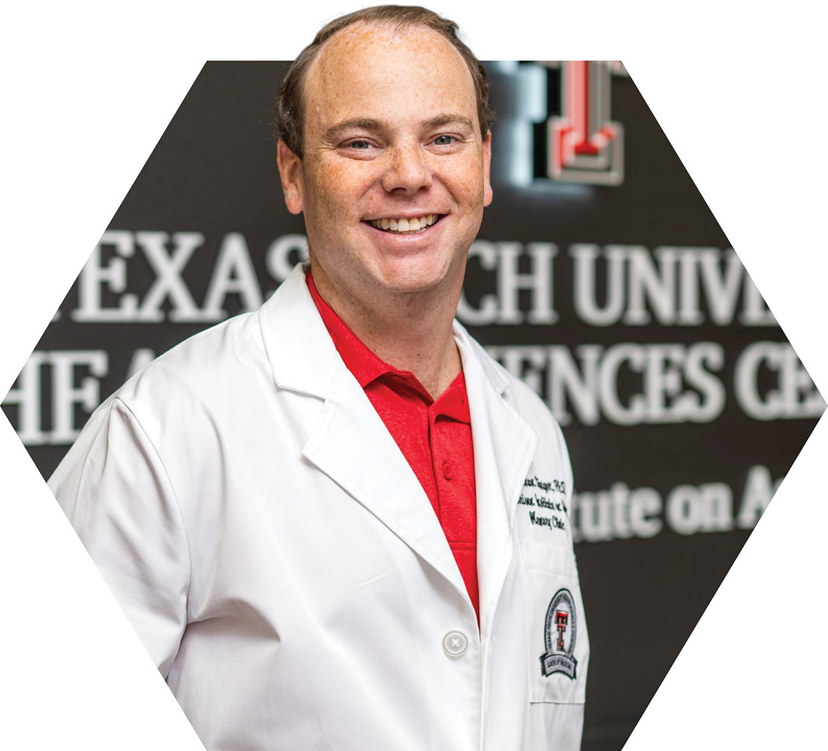 A doctor in a white lab coat smiling in front of a Texas Tech University sign.