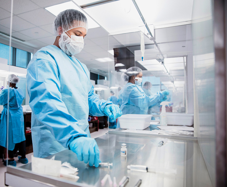 Laboratory personnel in blue sterile gowns and masks work inside a cleanroom hood environment.