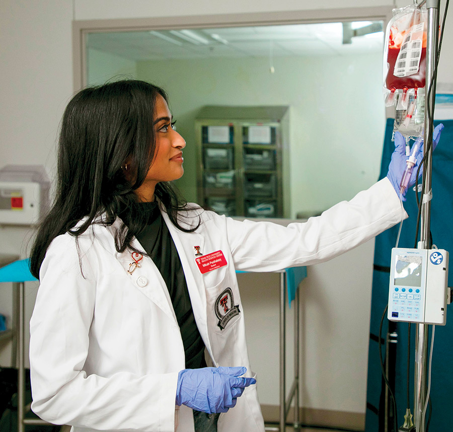 A medical student in a white coat adjusts an IV bag containing blood product.